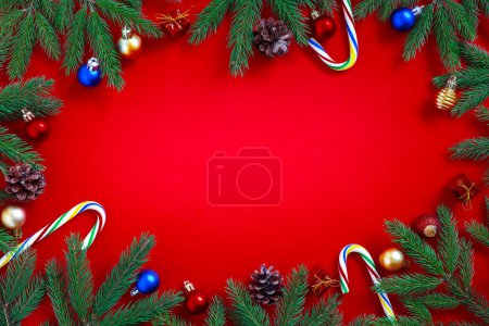 Foto de Adornos rojos navideños, bastón de caramelo, ramas de abeto y bolas de Navidad sobre fondo rojo. Piso tendido, vista superior, espacio para copiar. Composición navideña. - Imagen libre de derechos