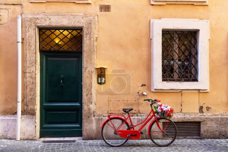 Foto de Imagen de una bicicleta roja en una antigua calle empedrada estrecha en Roma, Italia. Calle antigua en Roma, Italia. Arquitectura y punto de referencia de Roma. - Imagen libre de derechos