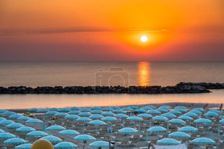 Schöner Sonnenaufgang mit Sonnenreflexion am Strand von Rimini mit Sonnenschirmen