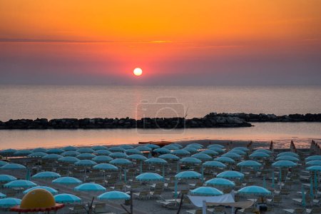 Beautiful sunrise with sun reflection on Rimini beach with umbrellas