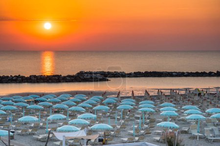 Hermoso amanecer con reflejo de sol en la playa de Rimini con sombrillas