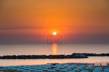 Beautiful sunrise with sun reflection on Rimini beach with umbrellas