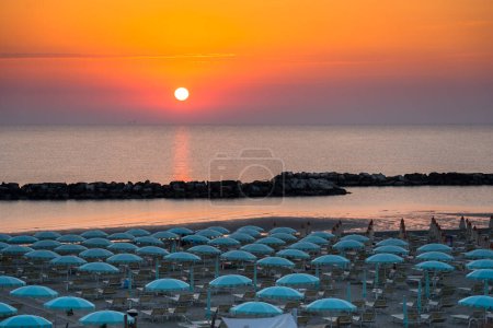 Schöner Sonnenaufgang mit Sonnenreflexion am Strand von Rimini mit Sonnenschirmen