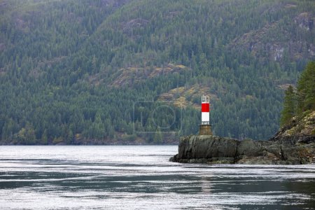 Ein rot-weißer Turm steht wie ein Leuchtturm inmitten eines riesigen Gewässers und fungiert als Leuchtturm für Schiffe, die die Küsten- und Ozeanlandschaften befahren.