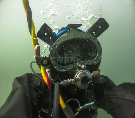 Buzo comercial en casco trabajando en primer plano bajo el agua