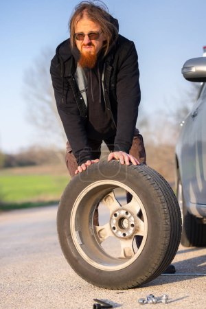 Hombre sosteniendo neumático de repuesto en el primer plano de la parada de carretera