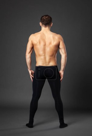 Full-length portrait of a young ballet dancer photographed from behind, standing in front of a gray background.