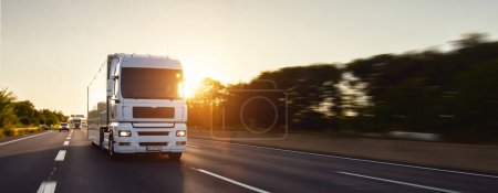 Photo for Cargo truck with cargo trailer driving on a highway. White Truck delivers goods in early hours of the Morning - very low angle drive thru close up shot. - Royalty Free Image