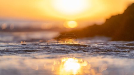 Téléchargez les photos : Gros plan des vagues frappant une pierre à la plage au coucher du soleil calme orange océan. focus sélectif - en image libre de droit