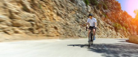 Foto de Hombre Adulto en una bicicleta de carreras escalando la colina en el paisaje marino mediterráneo carretera costera en mallorca isla baleárica - Imagen libre de derechos