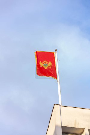 The national flag of Montenegro floating against the blue sky in the capital city, Podgorica.