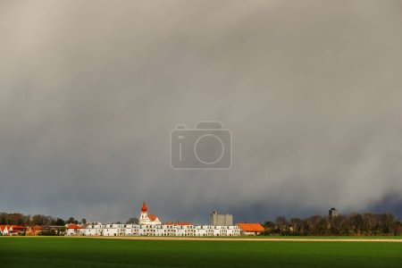 Photo for Dense rain over a church and white houses and fresh green fields in the foreground - Royalty Free Image