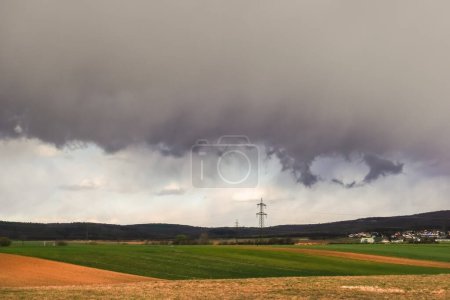 Photo for Dense gray rain clouds during a storm over fields and electric pylons in the landscapce - Royalty Free Image