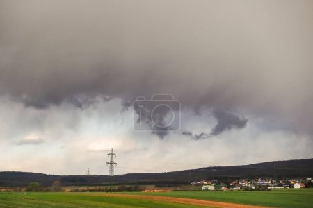 Photo for Heavy gray rain clouds over a nature landscape with forest houses and fields - Royalty Free Image