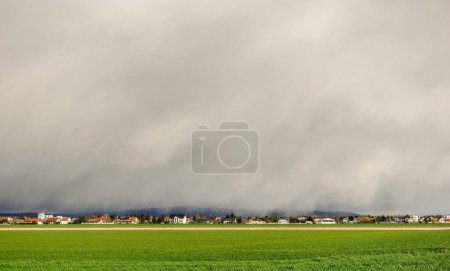 Photo for Dense rain over a village and a fresh green meadow in the foreground the spring - Royalty Free Image