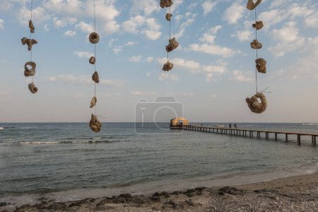 Foto de Gran cantidad de conchas y corales colgados en una cuerda en la playa con un embarcadero largo en Egipto - Imagen libre de derechos
