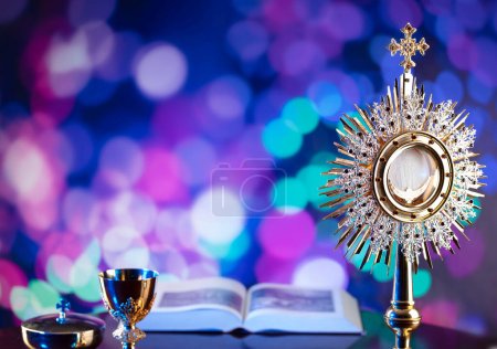 Photo for Catholic religion concept. Catholic symbols composition. The Cross, monstrance,  Holy Bible, rosary and golden chalice on blue bokeh background. - Royalty Free Image