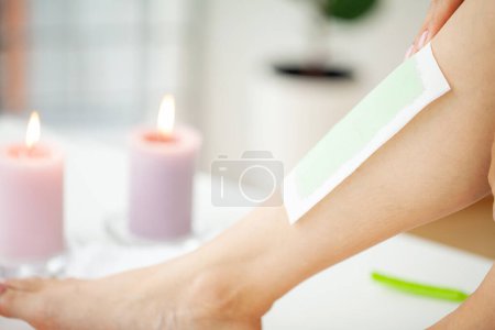 Téléchargez les photos : Jeune femme épilant sa jambe avec une bande de cire à la maison
. - en image libre de droit