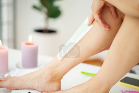 Téléchargez les photos : Femme utilisant une bande de cire d'abeille pour se raser la jambe
. - en image libre de droit