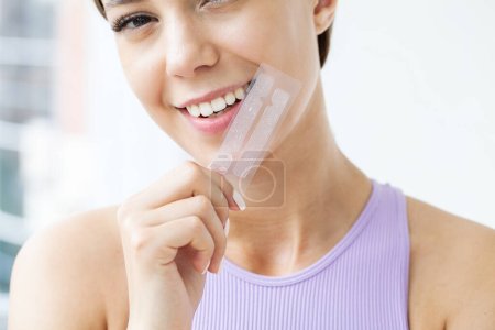 Schöne junge Mädchen mit weißen Zähnen Halten in den Händen Streifen für Zahnaufhellung