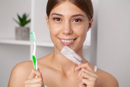 Foto de Blanqueamiento de dientes, hermosa mujer sonriente sosteniendo tira blanqueadora - Imagen libre de derechos