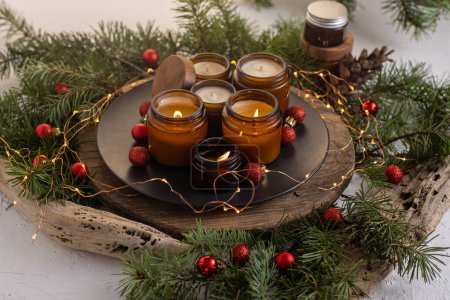 Photo for Soy candles burn in glass jars. Comfort at home. Candle in a brown jar. Scent and light. Scented handmade candle. Aroma therapy. Christmas tree and winter mood. Cozy decor. Festive garland decoration - Royalty Free Image