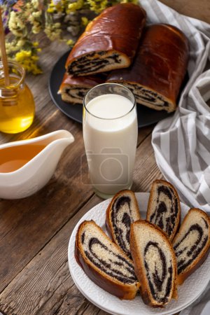 Téléchargez les photos : Roll with poppy seeds and a glass of milk. Food on the table. Sweet sweet pastries. Homemade simple yeast bun with filling. Breakfast on a wooden table. lactose and gluten. Honey spas - en image libre de droit