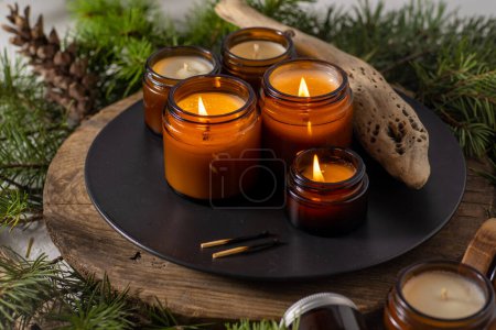 Photo for Soy candles burn in glass jars. Comfort at home. Candle in a brown jar. Scent and light. Scented handmade candle. Aroma therapy. Christmas tree and winter mood. Cozy decor. Festive decoration - Royalty Free Image