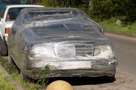 Photo for The passenger car is packed in a plastic bag made of stretch film and stands on the street. Storage is an alternative to a garage. Vandalism and revenge. Disposal of packaging. Humor - Royalty Free Image