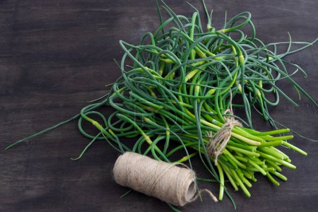 Photo for Garlic arrows. A bunch of greens on the table. Vegetable healthy vitamin food. Green stem stalks seedlings for salad and stewing. Vegetarian fresh herbs, chinese cuisine. - Royalty Free Image