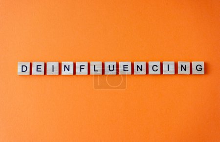 Photo for Word deinfluencing. The phrase is laid out in wooden letters top view. Motivation. Orange flat lay background - Royalty Free Image