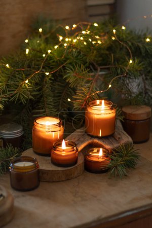 Sojakerzen brennen im Glas. Komfort zu Hause. Kerze in einem braunen Glas. Duft und Licht. Duftende handgemachte Kerze. Aromatherapie. Weihnachtsbaum und Winterstimmung. Gemütliche Wohnkultur. Festliche Dekoration.