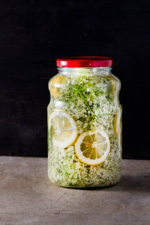 Elder flowers drink juice glass. White flower and lemon. Harvesting buds for making syrup and drink at summer. Cooking and food on the table. Sambucus plant in jar.