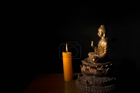 Buddha statue with a burning candle on black background