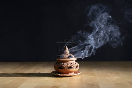 Räucherstäbchen brennen auf einem Räucherofen auf dem Tisch, mit dunklem Hintergrund. Religionskonzept.