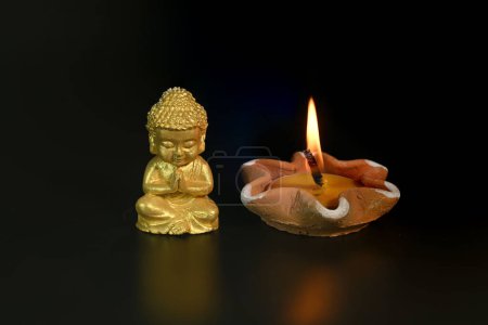 Close-up of a little Buddha statue and burning candles on a black background