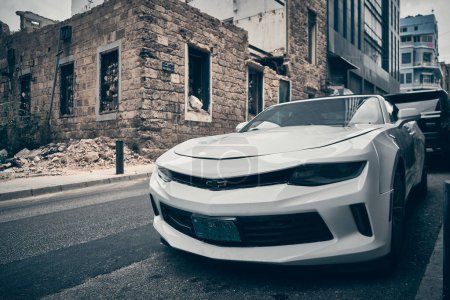 Photo for White Chevrolet Camaro parked on a city street opposite ruined residential building. Beirut, Lebanon - May 2023 - Royalty Free Image