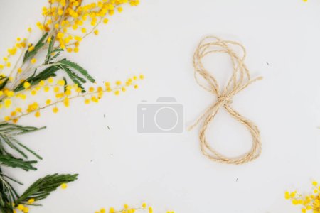 Foto de El 8 de marzo son unas vacaciones de primavera. El número 8 hecho de cuerda yace sobre un fondo blanco de cerca. Cerca se encuentra una rama de mimos amarillos - Imagen libre de derechos