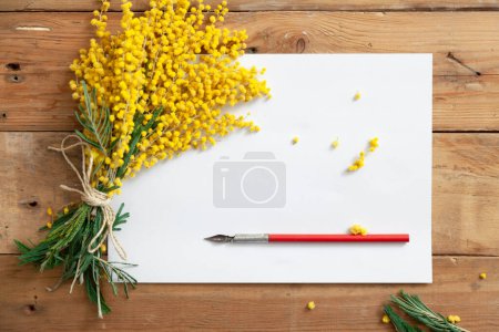 Foto de Romántico juego de primavera para escribir. Un ramo de mimosa amarilla y una pluma de tinta vintage se encuentran en una hoja de pape blanco - Imagen libre de derechos