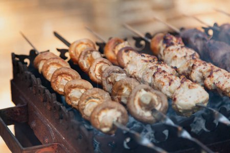Photo for Grilling a barbecue. On a metal grill lies a row of skewers with mushrooms and pieces of mea - Royalty Free Image