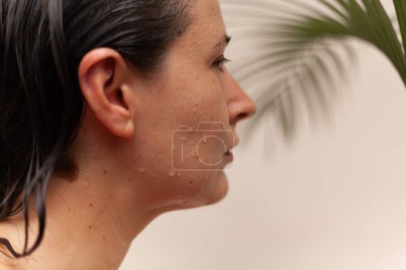 Téléchargez les photos : Portrait d'une jolie femme slave avec des gouttes d'eau sur le visage. Branche floue de palmier vert dans le backgroun - en image libre de droit