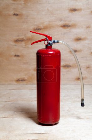 Photo for A red fire extinguisher stands against a background of light plywood. Structural stains are visible on a vertical plywood shee - Royalty Free Image