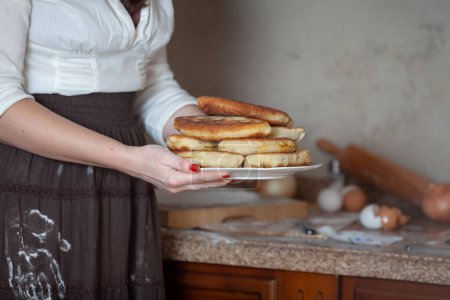 Photo for A woman holds a plate with delicious pies, there is a white flour handprint on a brown skirt - Royalty Free Image
