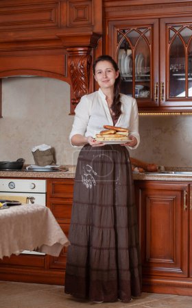 Photo for Cute brunette woman holding a plate with delicious pies, a white flour handprint on a brown skir - Royalty Free Image