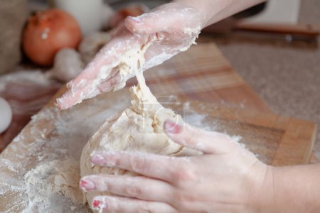 Photo for Handmade in the kitchen. The dough sticks to a woman hand while mixin - Royalty Free Image