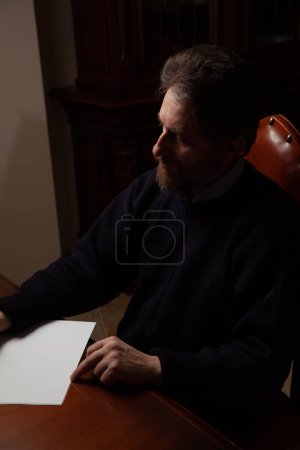 Ein Mann mit Bart schreibt einen Brief mit einem alten Holzstift mit einem Metallstift. In der Nähe befindet sich ein Tintenfass