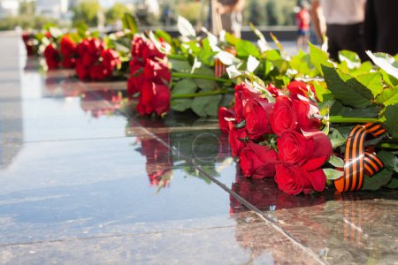 Sträuße roter Rosen liegen auf der Granitoberfläche des Denkmals zum Gedenken an die gefallenen Soldaten im Großen Vaterländischen Krieg in Moskau. Rosen sind mit St. George-Schleife in schwarz und orangen geschmückt