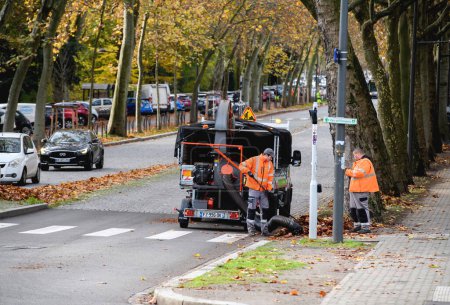 Photo for Strasbourg, France - Nov 22, 2022: Workers sweeping footpath during autumn using powerful vacuum cleaner to absorb debris and leaves - Royalty Free Image