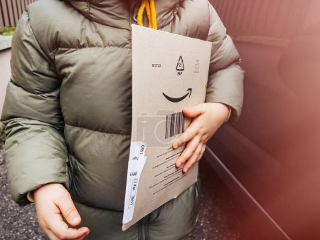 Téléchargez les photos : Luxembourg - 8 nov. 2022 : Un tout-petit homme tient Amazon Prime carton boîte de colis carton - livraison rapide chez le détaillant en ligne - en image libre de droit