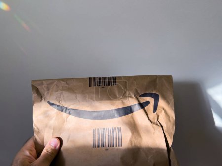 Photo for Paris, France - Oct 4, 2022: POV male hand holding Amazon prime cardboard parcel paper recycled bag with large smiling arrow - white abstract background - Royalty Free Image
